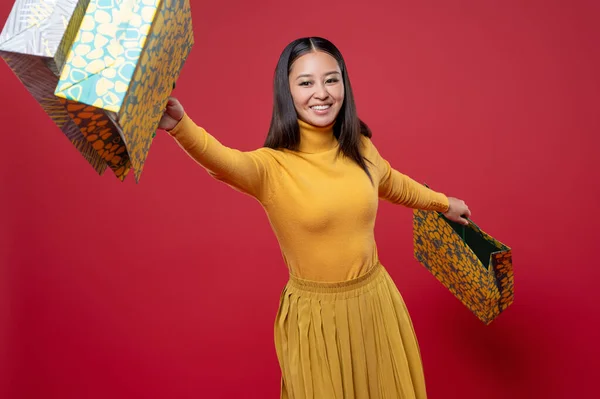 Merry Fashionista Zwaaien Haar Boodschappentassen Voorkant Van Camera Rode Achtergrond — Stockfoto