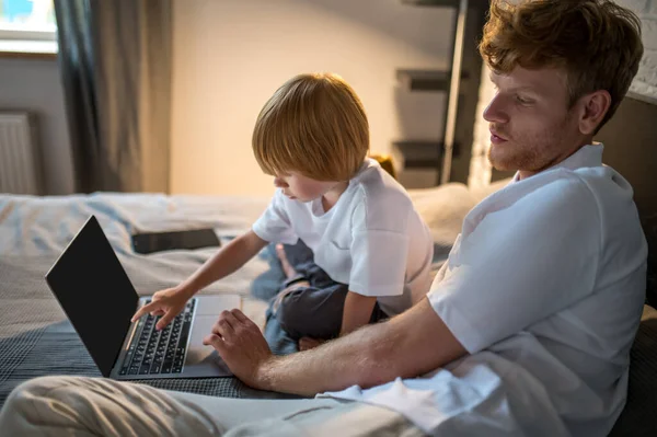 Watching something online. Dad and son lying in bed and watching something online before sleep