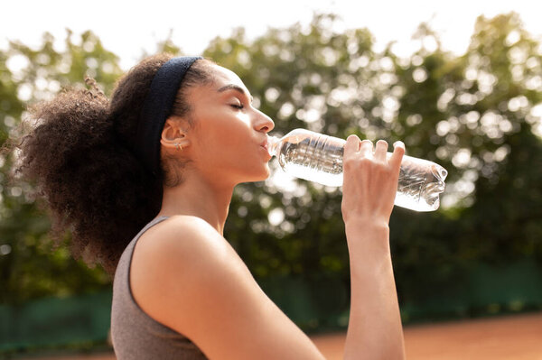 Feeling thirsty. Pretty young girl drinking water after exercising