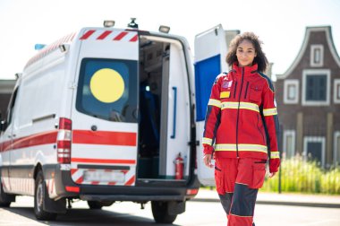 Kırmızı üniformalı genç Afrikalı acil servis doktoru ambulans minibüsünden uzaklaşıyor.