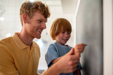 Öğrenme süreci. Babam küçük bir çocuğa tahtaya yazı yazmayı öğretiyor.