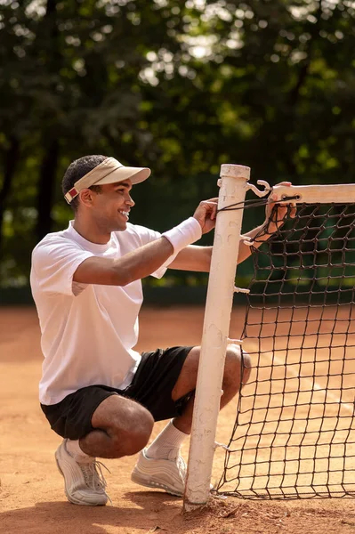 テニスコート 若いスポーツマンの笑顔テニスコートでネットを固定 — ストック写真