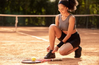 Tenis kortunda. Genç kız maçtan önce ayakkabılarını bağlıyor.