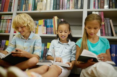 Birlikte okuyoruz. Kütüphanede yerde oturmuş kitap okuyan bir grup çocuk.