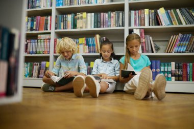 Birlikte okuyoruz. Kütüphanede yerde oturmuş kitap okuyan bir grup çocuk.