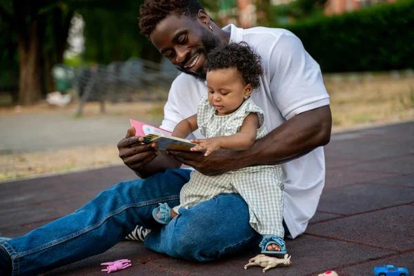 彼女の幸せな親の膝の上に座っている子供は彼の手の中にオープン本に触れて — ストック写真