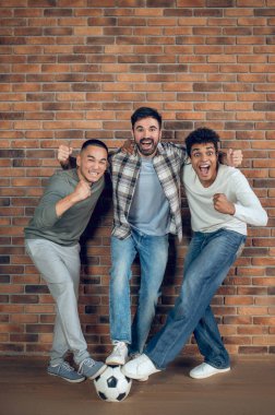 Neşeli adam ve neşeli arkadaşları ayaklarını futbol topuna basarken yumruk sallıyorlar.