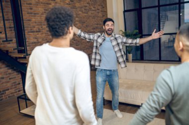 Gülümseyen, mutlu, misafirperver bir adam. Oturma odasında kollarını açmış iki arkadaşına hoş geldin diyor.