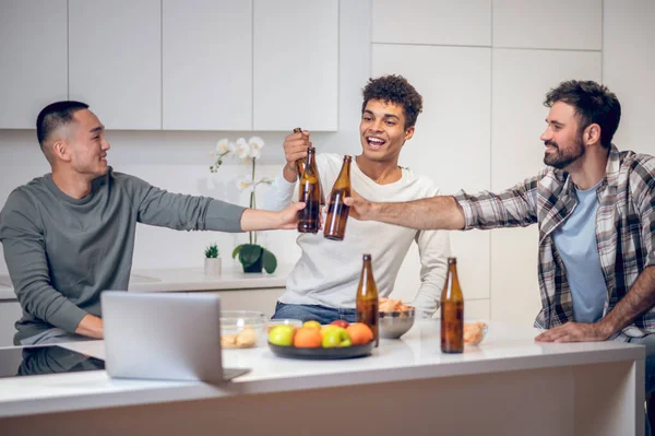 Alegre Compañía Tres Amigos Multiétnicos Sentados Mesa Tintineando Botellas Cerveza — Foto de Stock