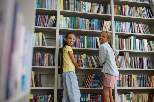 School library. Girls standing near the high book shelves in the school library