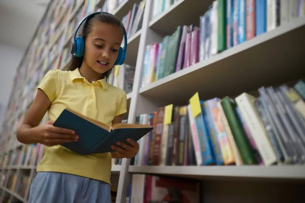 Modern Okul Çocuğu Kulaklıklı Kız Kütüphanede Kitap Okuyor — Stok fotoğraf