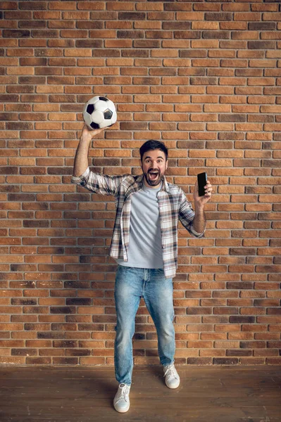 Plnohodnotný Portrét Křičícího Chlapa Držícího Fotbalový Míček Mobilní Telefon Zdvižených — Stock fotografie