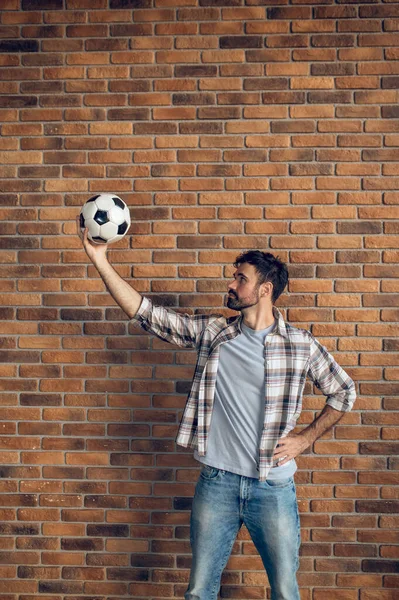 Серьезный Темноволосый Бородатый Молодой Кавказский Мужчина Смотрит Футбольный Мяч Поднятой — стоковое фото