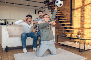 Bir odada TV 'de futbol maçı izleyen üç genç çoklu etnik arkadaş.