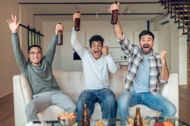 Kanepede oturan arkadaşlar TV izlerken bağırıp çağırıyorlardı.