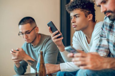 Ciddi şekilde odaklanmış yakışıklı, koyu renk saçlı bir Arap ve iki arkadaşı cep telefonlarını kullanıyor.