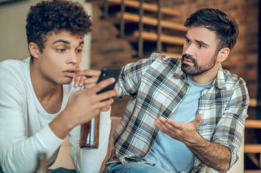 Ciddi esmer sakallı genç adam konuşma sırasında üzgün arkadaşının omzuna hafifçe vuruyor.