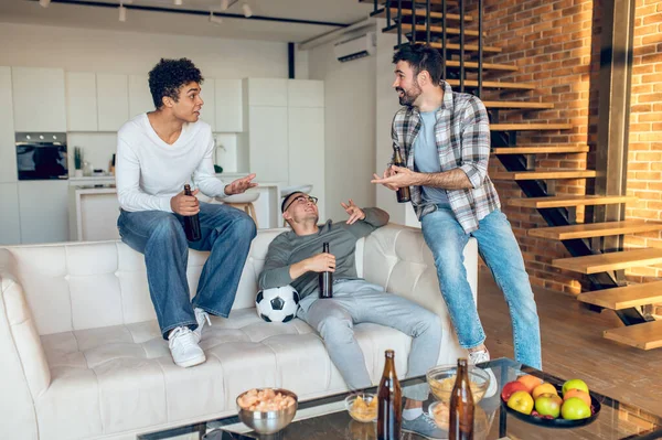 Sonriendo Contento Joven Sentado Sofá Con Una Botella Cerveza Escuchando — Foto de Stock