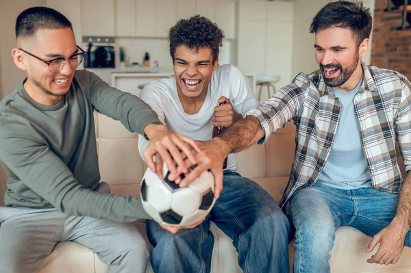 Company Cheerful Young Men Seated Sofa Putting Hands Football — Stock Photo, Image