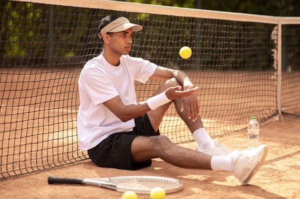 テニスコート 若いですハンサムなテニスプレーヤー座っていますテニスコートに手にテニスボール — ストック写真