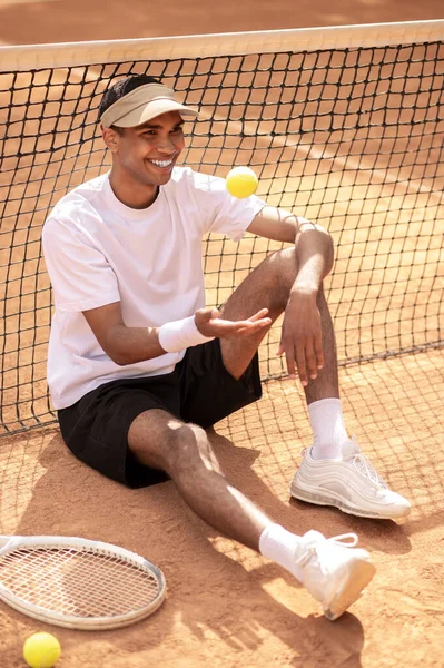 网球场 年轻英俊的网球选手手拿着网球坐在网球场上 — 图库照片