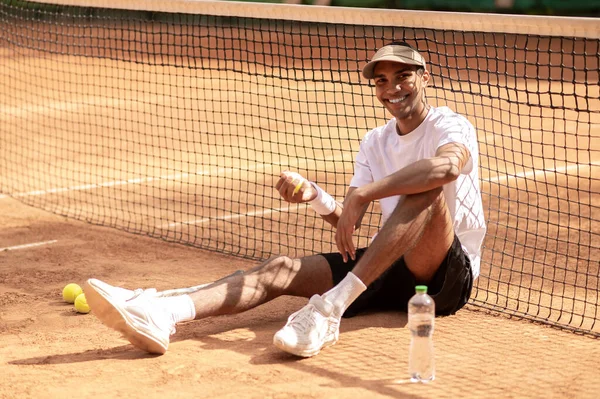 网球场 年轻英俊的网球选手手拿着网球坐在网球场上 — 图库照片