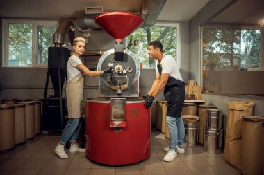 Dişi rosto ustası memnun iş arkadaşının huzurunda kaşık örneğini kahve kızartma makinesinden alıyor.