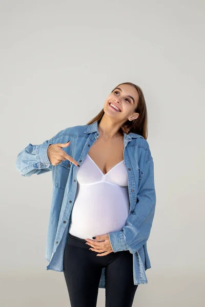 快乐的妈妈年轻的孕妇指着她的大肚子 看上去很开心 — 图库照片