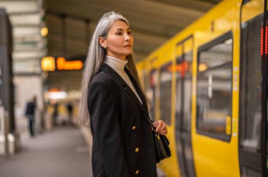 Metroda. Uzun saçlı, siyah paltolu bir kadın metroda tren bekliyor.