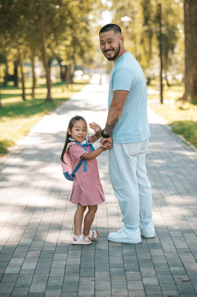 Time together. Little girl with backpack and her father in the park