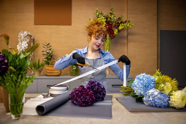 仕事中の花屋さん かわいい生姜の花屋は花束のためのカバーを作りながら関与見て — ストック写真