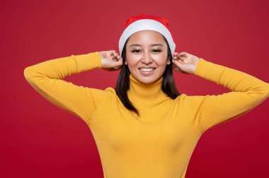 Gülümsüyor ve mutlu. Noel Baba şapkalı sevimli Asyalı genç kadın.