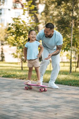 Kaykay tahtası. Baba kızına kaykay sürmeyi öğretiyor.