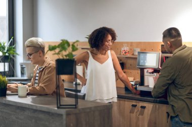 Kadın meslektaşı iş arkadaşını kahve yaparken seyrederken konsantre bir şirket çalışanı dizüstü bilgisayarda daktilo yazıyor.