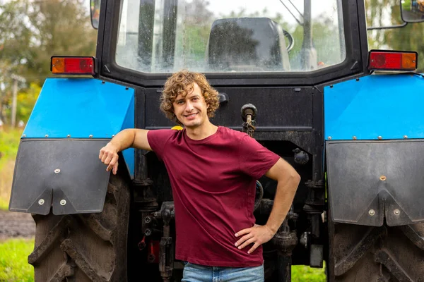 年轻的农业工人靠在拖拉机上 望着前面 笑得很开心 — 图库照片