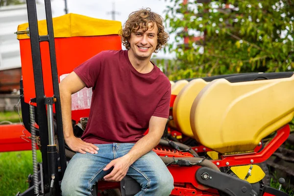 在外面坐在稻草机上摆出一副对着摄像机的样子 笑笑着年轻的白人农业工人 — 图库照片