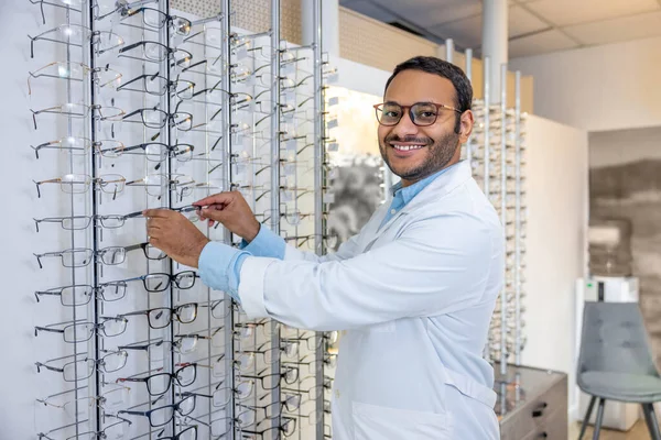 Eyeglasses for you. Smiling male consultant in lab coat selling eyeglasses