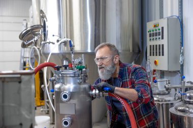 Çalışıyorum. Koruyucu gözlüklü yetişkin bir adam fabrika ekipmanı üzerinde çalışıyor.