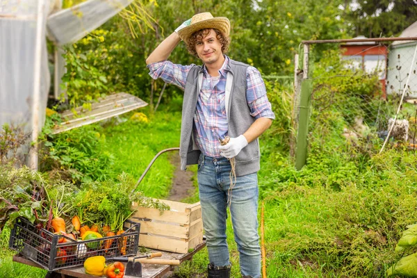 新鮮な野菜を積んだカートの横に立っているわらの帽子で幸せな農家を微笑む — ストック写真
