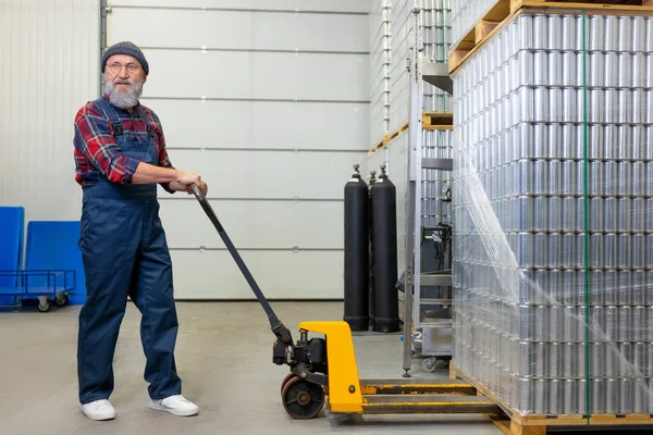 Full-length portrait of a warehouse loader pushing the pallet jack with stacked drink aluminum cans
