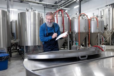 Not alıyorum. Sakallı fabrika işçisi bira fabrikası sürecinde notlar alıyor.