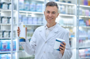 Infant milk. Smiling male pharmacist with cans of infant milk in hands