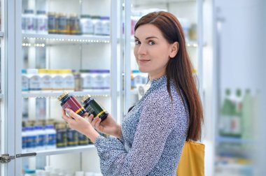 Choosing vitamins. Dark-haired woman buying vitamins at the drugstore