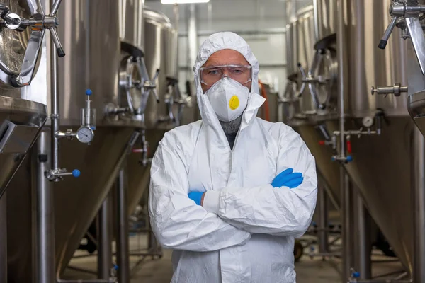 Waist-up portrait of a serious brewer in protective clothing posing for the camera in the factory