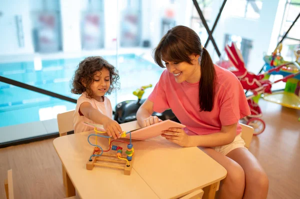 Play room. Young dark-haired woman playing with her kid in a play room