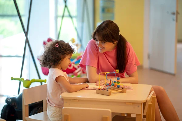 Play room. Young dark-haired woman playing with her kid in a play room