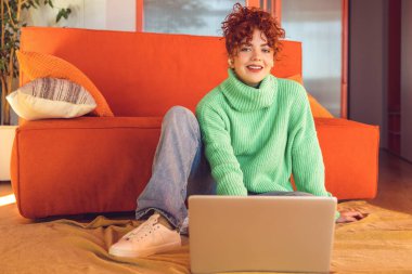 Freelance. Ginger girl in green sweater sitting on the floor at the laptop