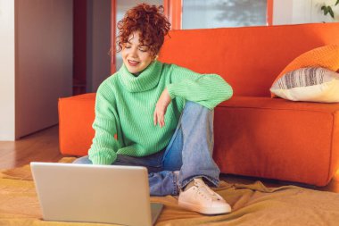 Freelance. Ginger girl in green sweater sitting on the floor at the laptop