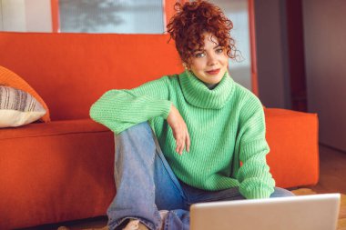 Freelance. Ginger girl in green sweater sitting on the floor at the laptop