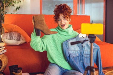 Internet shop. Ginger young girl demonstrating and selling clothes online